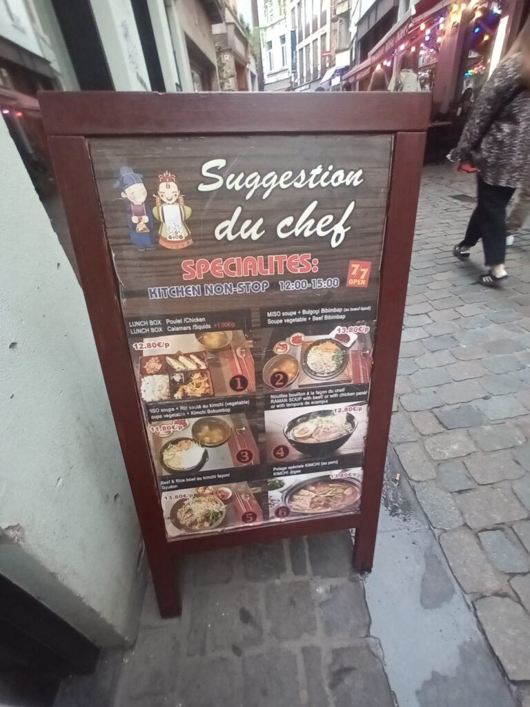 Cartel del menú coreano del restaurante Chez Kimchi en una calle peatonal de Bruselas.